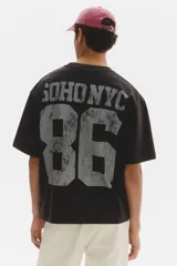 Remera de algodón en punto pesado color negro, de corte holgado con hombros caídos, cuello redondo acanalado y estampa frontal estilo universitario con el texto 'SOHO NYC 86'.