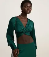 Blusa cropped satinada color verde esmeralda, con escote en V, manga larga con puños drapeados y nudo en el busto.