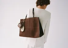 Bolso tipo shopper de piel de serraje en color marrón, con diseño de paneles y doble asa de hombro. Cuenta con cierre de botón magnético y bolsillo interior con cremallera.