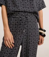 Pantalón carrot de crepé con cintura alta, estampado geométrico en blanco y negro, y lazo en la cintura.
