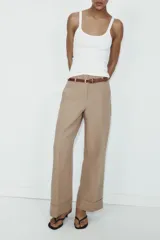 Pantalón de tiro alto color marrón, de corte recto y holgado, con bajo acabado en vuelta. Incluye bolsillos delanteros y cinturón fino a contraste con hebilla metálica.