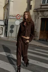 Chaqueta de cuello solapa y manga larga, color marrón oscuro, con efecto ante. Presenta bolsillos delanteros de plastrón, cierre frontal con botones y un bajo troquelado con diseño floral y acabado festoneado.