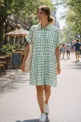 Vestido camisero de corte holgado y silueta relajada, con cuello clásico, cierre frontal de botones y mangas cortas con dobladillo. Presenta un estampado geométrico de cuadrícula en tonos verde agua y blanco.