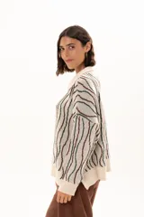 Buzo de tejido de punto con diseño de rayas verticales onduladas en tonos verde y marrón sobre base color crudo. Presenta cuello tipo polo con cierre frontal de botones y mangas largas con puños acanalados.