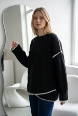 Sweater de punto gris con textura suave, diseño oversize, cuello redondo y detalles de costuras expuestas en color blanco en mangas y ruedo.