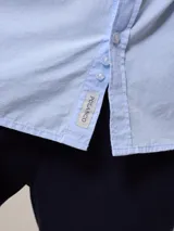 Camisa de manga larga para hombre, confeccionada en algodón con efecto peach (textura suave). Presenta un estampado de cuadros vichy en tonos azul marino y blanco, cuello con botones y un bolsillo de parche en el pecho izquierdo.