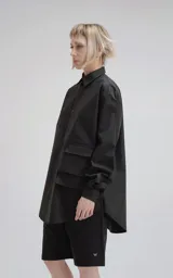 Camisa negra de manga larga, confeccionada en poplín de algodón. Presenta un calce oversize, cuello camisero, cierre frontal de botones y dos bolsillos cuadrados superpuestos en el lado derecho del pecho.