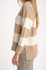 Sweater de punto con diseño de rayas horizontales anchas en tonos beige y crema, con textura jaspeada. Presenta cuello redondo, mangas largas con puños acanalados y un corte holgado.
