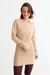Vestido corto de tejido de punto color beige, con cuello polo y mangas largas. Presenta un diseño de textura acanalada en la parte inferior y lisa en la parte superior.