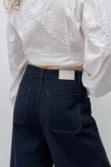 Jean wide leg negro de tiro alto, confeccionado en denim rígido, con diseño de cinco bolsillos, presillas para cinto, cierre frontal con botón y ruedo desflecado.