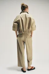Trench corto de color beige, con cuello de solapa, cierre cruzado con botones y mangas cortas con vuelta y trabilla con botón.