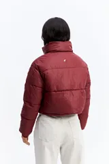 Campera puffer de corte cropped, color marrón oscuro, con cuello alto, cierre frontal con cremallera y botones a presión, y puños elásticos.