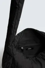 Bolso de hombro confeccionado en tejido técnico acolchado de color negro. Presenta un diseño de solapa con cierre magnético y cremallera, asa de hombro integrada y compartimentos interiores.