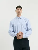 Camisa de manga larga con estampado de rayas verticales en azul y blanco, cuello clásico y bolsillo frontal.