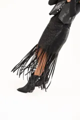 Pollera midi de cuerina negra con diseño ajustado en la parte superior y terminación en flecos largos que aportan movimiento.