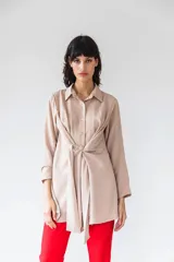 Camisa manga larga color beige con textura plumetie, abotonada en el pecho y lazo regulable que permite múltiples usos.