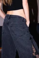 Jean negro de corte relajado, confeccionado en denim con inserciones laterales de encaje negro translúcido y detalles brillantes.