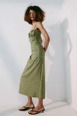 Vestido midi verde militar con estampado de lunares rosados, de corte recto y tirantes finos cruzados en la espalda. Presenta escote con frunces y detalle de lazo en el centro.