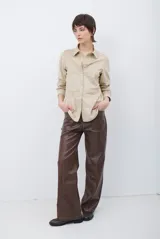 Camisa de estilo casual confeccionada en material tipo gamuza color marrón, con cuello clásico, cierre frontal con botones y costuras a la vista en tono contrastante.