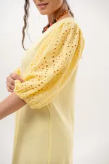 Vestido largo amarillo mantequilla con escote en V, mangas abullonadas y volados en el bajo con detalles de broderie.