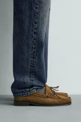 Mocasín de vestir para hombre confeccionado en piel con acabado en gamuza de color marrón, con punta redonda, suela oscura con ligero tacón y detalle de lazo en el empeine.