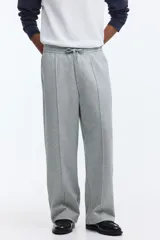 Pantalón jogger de punto de algodón gris melange, de corte relajado y perneras rectas con pliegue frontal cosido. Presenta cintura elástica con cordón ajustable, bolsillos laterales y falsas braguetas decorativas.