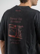 Remera oversize de algodón color negro con efecto lavado. Presenta un estampado gráfico en la espalda con la frase 'Freeze the moment' y un diseño de cámara fotográfica en tonos rojizos.