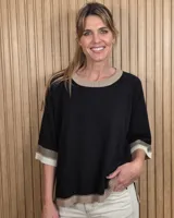 Buzo de punto negro con diseño holgado, mangas codo y detalles en tono tostado y blanco en el cuello redondo, puños y ruedo.