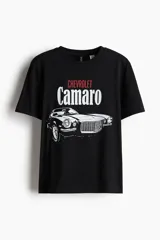 Remera negra de algodón con cuello redondo y mangas cortas. Estampado frontal con el logo de Chevrolet en rojo, la palabra Camaro en blanco y la silueta de un Chevrolet Camaro clásico en blanco y negro.