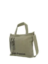Cartera tipo tote bag de canvas en color verde oliva, con estampado frontal de un perro basset hound y logo de la marca. Cuenta con doble asa de mano, correa ajustable extraíble, cierre principal de cremallera y bolsillos internos y traseros con cierre.