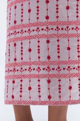 Vestido camisero de lino color lila con bordados rojos en contraste. Presenta un diseño de largo midi con cuello camisero, cierre frontal de botones y mangas cortas. Los detalles bordados recorren la botonadura, los puños y el ruedo de la prenda.