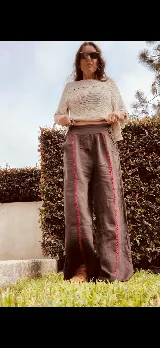 Pantalón ancho de lino color tostado, con cintura elástica y detalles de bordado rojo a lo largo de las piernas.