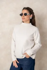 Buzo de punto color visón con cuello alto, manga larga y diseño holgado. Presenta un bordado floral en relieve al tono en la parte frontal.