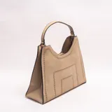 Cartera Xavielle de diseño estructurado trapezoidal en color beige, confeccionada en material sintético con efecto gamuza. Presenta detalles de perforaciones geométricas en los bordes y el centro, con un asa corta superior y cierre principal.