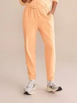 Pantalón estilo jogger color durazno, confeccionado en tejido con efecto plush de tacto suave y aterciopelado. Presenta cintura elástica con ajuste mediante amarre, bolsillos laterales y puños elásticos en los tobillos.