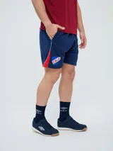 Bermuda deportiva Umbro del Club Nacional de Football, modelo Nexo para hombre, en color azul marino con detalles en rojo y blanco. Cuenta con el escudo del club bordado en la pierna derecha y el logo de Umbro en la izquierda, además de cordón ajustable en la cintura.