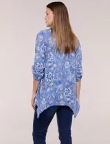 Blusa azul con estampado floral, escote en V, abotonadura frontal y mangas tres cuartos con presilla para arremangar. Cuenta con un diseño amplio y ruedo asimétrico en punta.