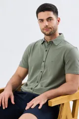 Camisa de piqué lisa color celeste, de manga corta, con cuello camisero y cierre frontal de botones oscuros.