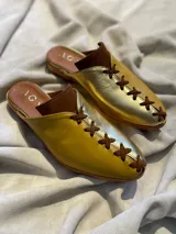 Zapatos tipo mules de punta cerrada y talón abierto, con diseño bicolor que combina cuero metalizado dorado y tono mostaza. Presentan detalles de costuras cruzadas en contraste sobre el empeine y suela baja.
