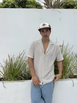 Camisa tejida a rayas verticales color beige y blanco, de corte recto, manga corta y cuello cubano.