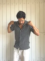 Camisa de hombre tejida a rayas verticales blancas y negras, de manga corta y cuello solapa.