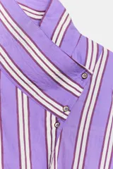 Camisa de corte oversize con diseño de rayas verticales en tonos violeta, blanco y bordó. Presenta cuello subido cruzado con cierre de botones frontal, mangas largas con puños y bajo asimétrico.
