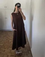 Vestido largo sin mangas, color marrón oscuro, con escote redondo y corte amplio. Presenta bolsillos laterales.
