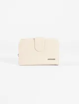 Billetera plegable color natural de cuero vegano con cierre perimetral y solapa con broche a presión. Cuenta con aplique metálico con el logo de la marca en el frente.