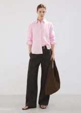 Camisa de lino color rosado, con diseño recto, cuello camisero, manga larga con puños abotonados y cierre frontal de botones.