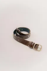 Cinturón de cuero marrón con textura desgastada, decorado con tachas metálicas en tonos dorados y plateados. Cuenta con una hebilla cuadrada de metal y presillas a juego.