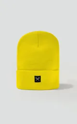 Gorro tejido de color amarillo brillante, estilo beanie con borde doblado y parche cuadrado negro con un logo bordado de tijeras cruzadas en blanco.