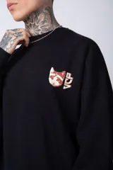 Buzo de tejido friza color crema, de corte oversize y cuello redondo. Presenta un pequeño bordado o parche en el pecho izquierdo con un diseño de cabeza de animal en tonos rojizos/terracota.