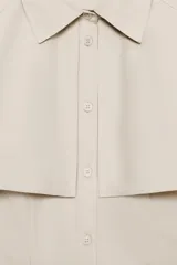 Vestido camisero midi de algodón con diseño de capa, cuello solapa, manga corta tipo capa y trabillas en los hombros. Presenta cierre frontal con botones, bolsillos delanteros y cinturón ajustable del mismo tejido con lazada. El bajo tiene un acabado en línea evasé.