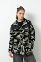 Campera de polar con estampado camuflado en tonos verde, gris y negro. Tiene cuello alto, cierre frontal y bolsillos laterales. La parte superior del pecho y los hombros son de tela lisa color negro.